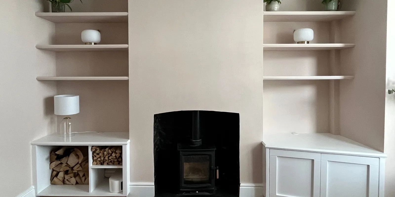 Asymmetrical custom alcove shelving and cabinets flanking a black wood burning stove fireplace with open log storage