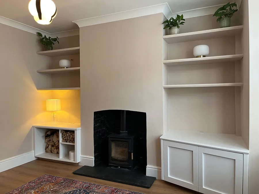Living room chimney breast with bespoke white alcove storage units, floating shelves, and illuminated table lamp