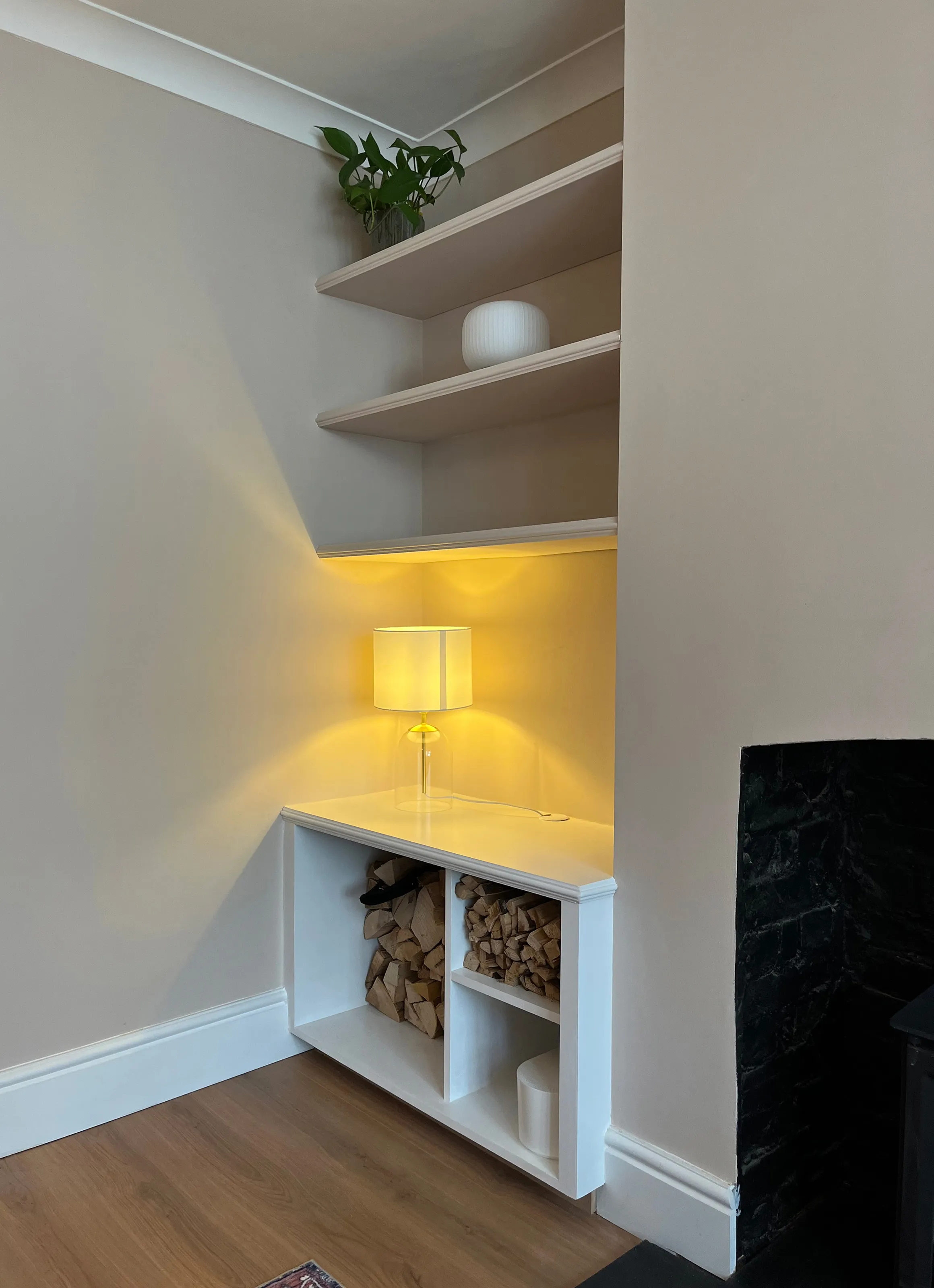 A left hand alcove unit showing three floating shelves and a segmented log store in the bottom unit