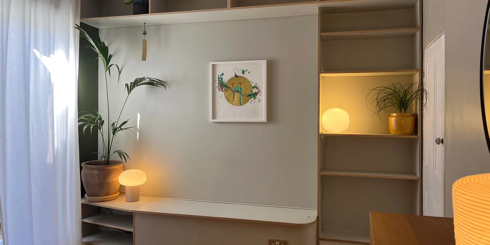 Custom built-in banquette seating unit with surrounding plywood shelves, warm accent lamps, and potted plants