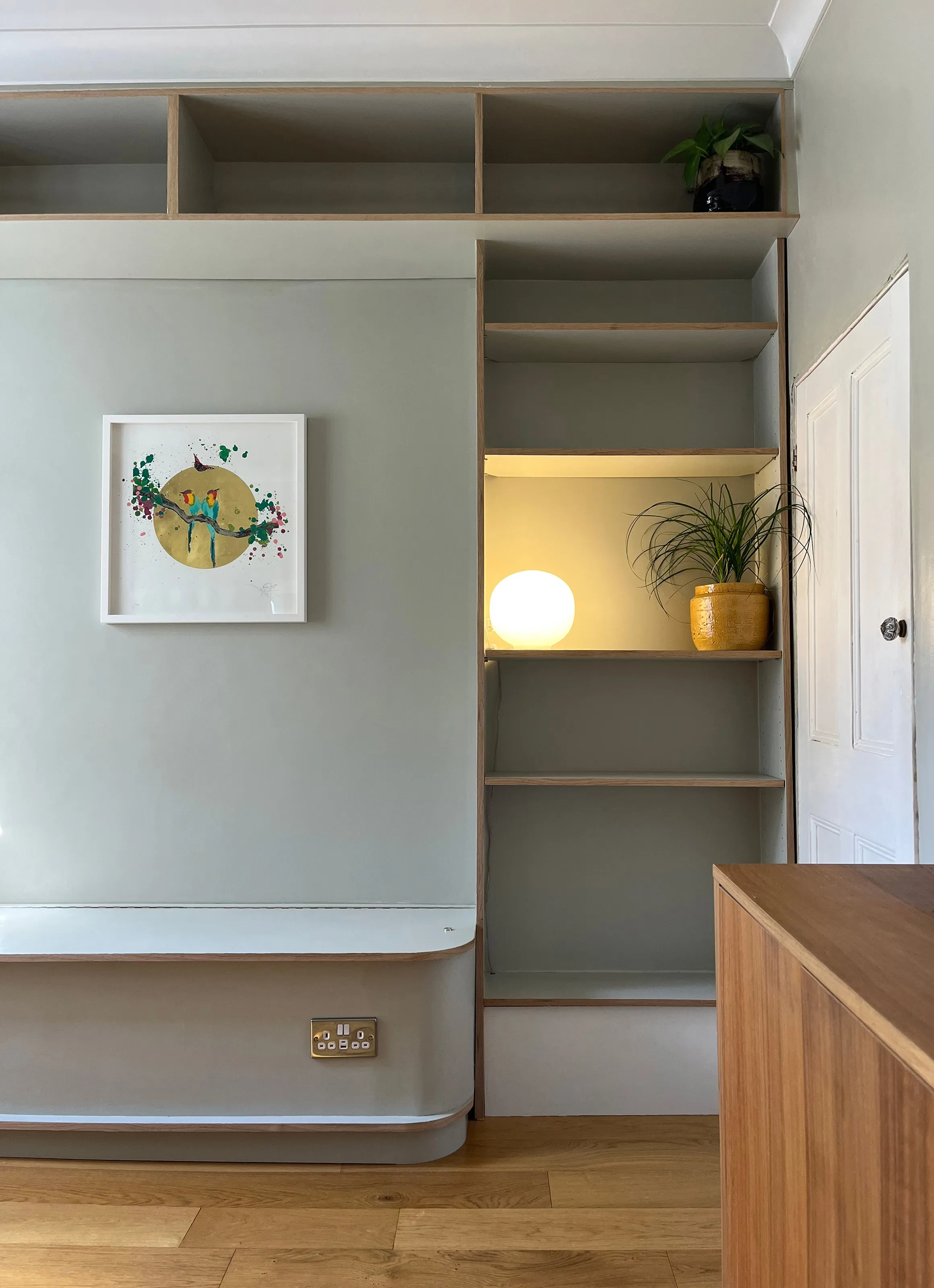 Custom plywood shelving tower with warm ambient backlighting alongside a built-in seating bench