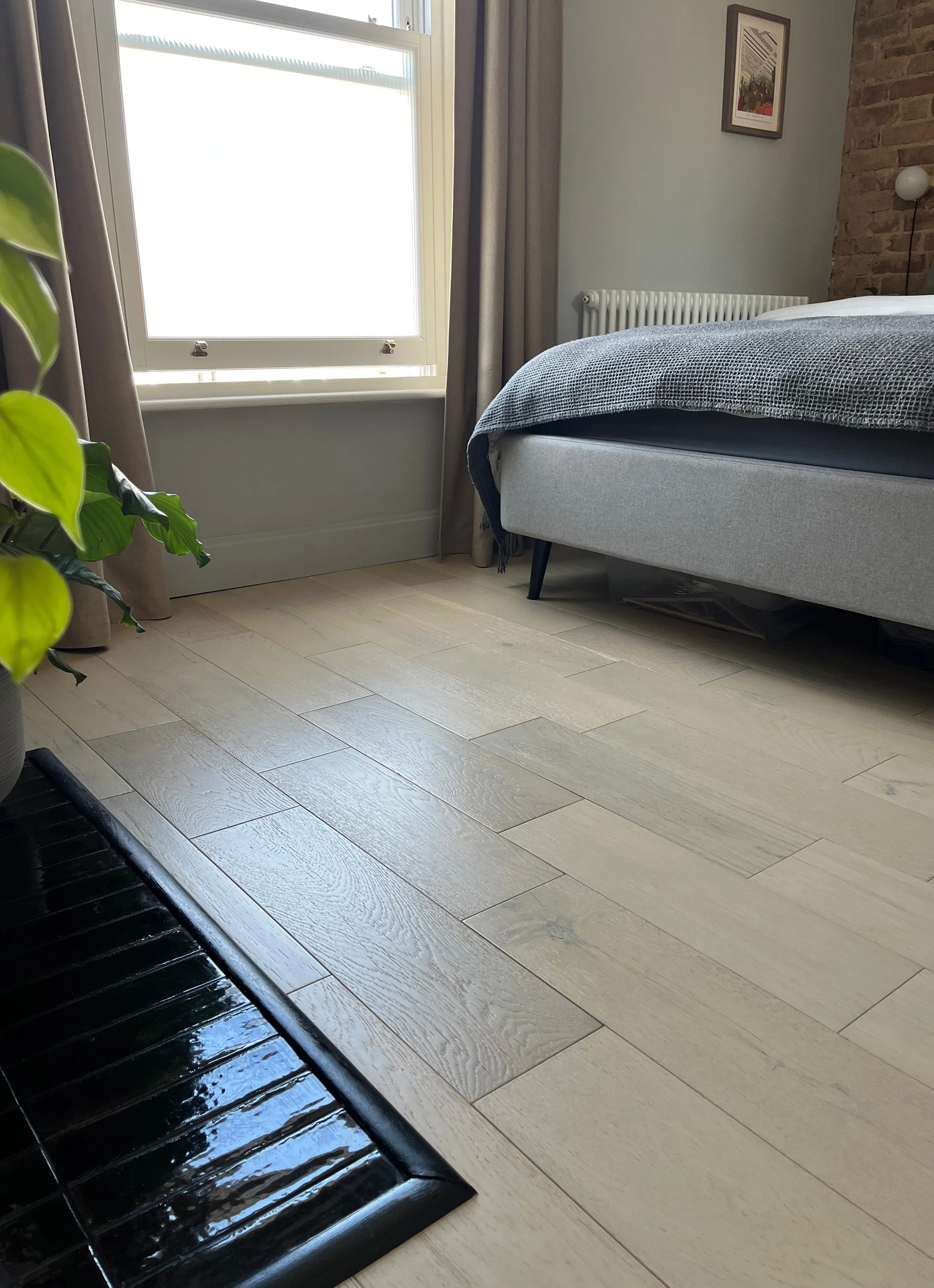 Light oak engineered wood flooring in a modern bedroom with exposed brick feature wall and window