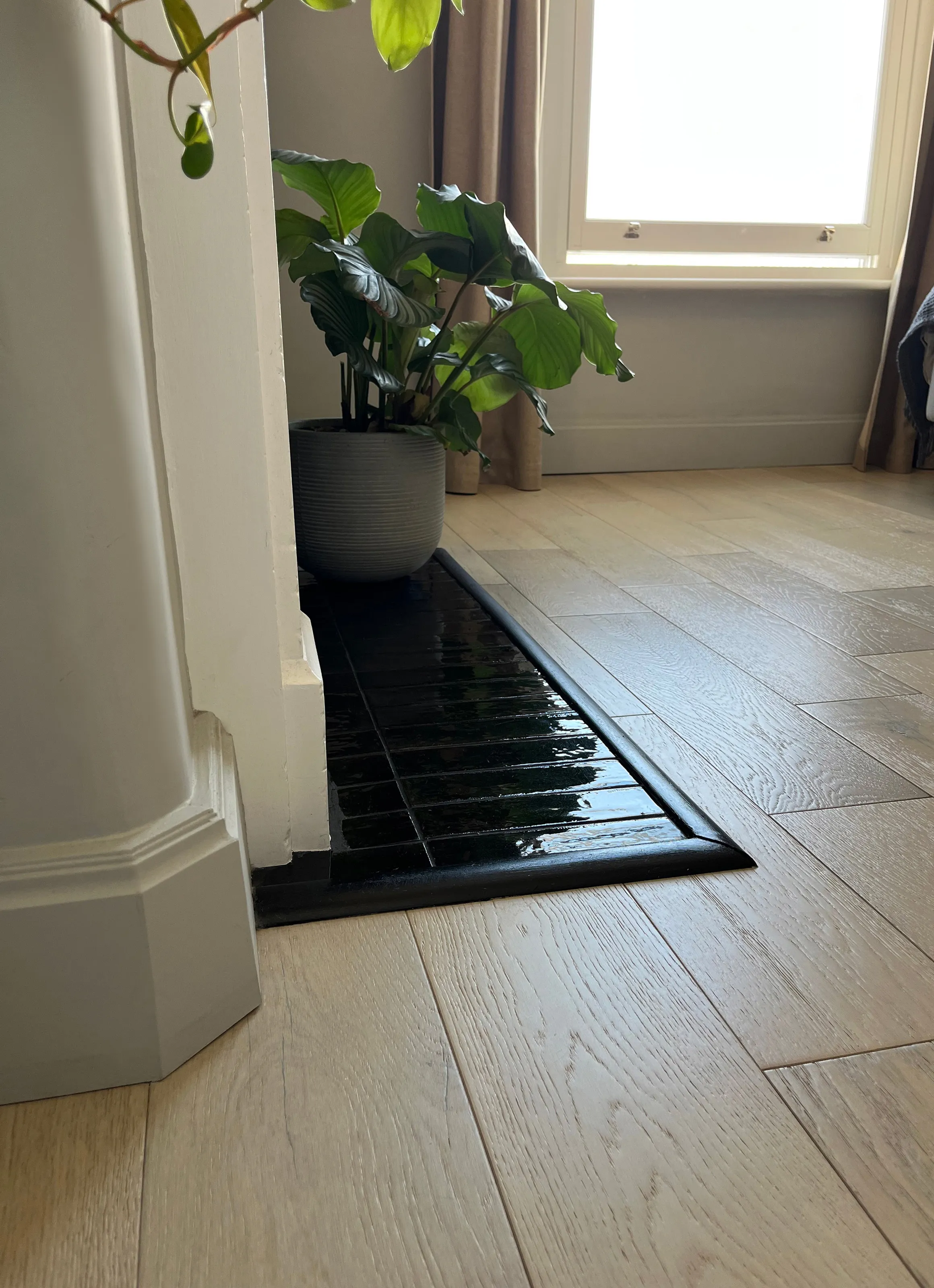 Close up of glossy black tile hearth transition to light wood floor planks in a modern bedroom