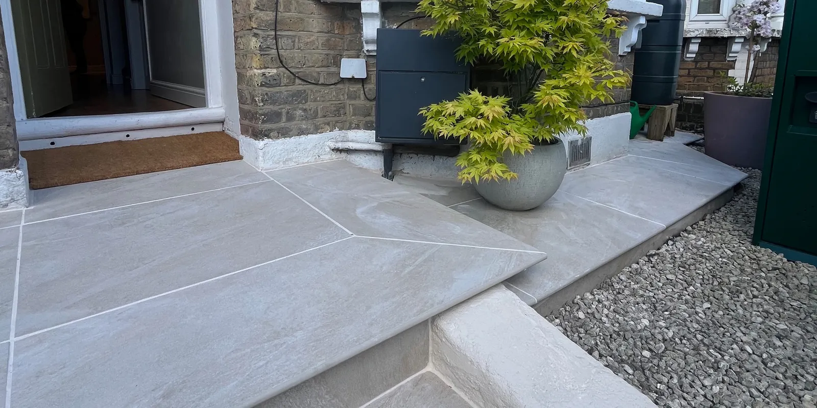 Newly installed light beige porcelain paving slab front porch step with potted Japanese maple tree near front door