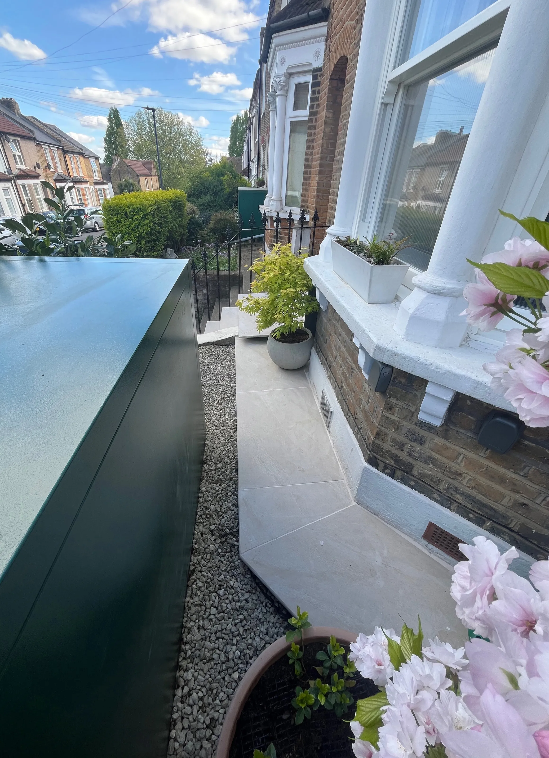 Modernized front garden path featuring light grey paving slabs, gravel border, and dark green storage shed