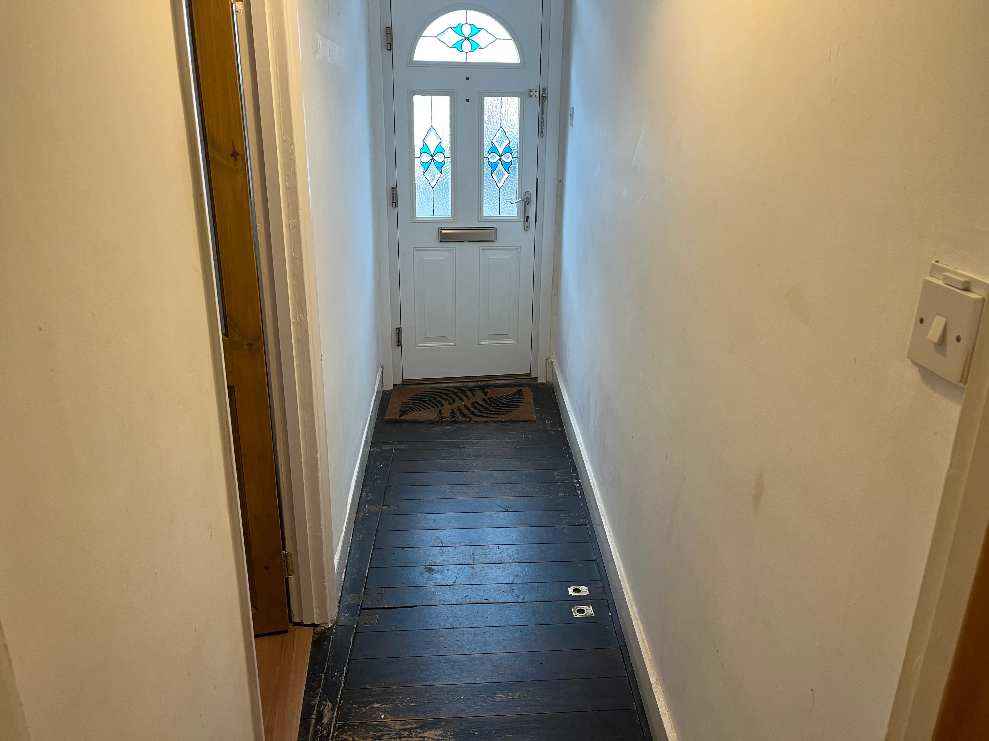 Before hallway renovation showing plain off-white walls, dark original floorboards, and front door