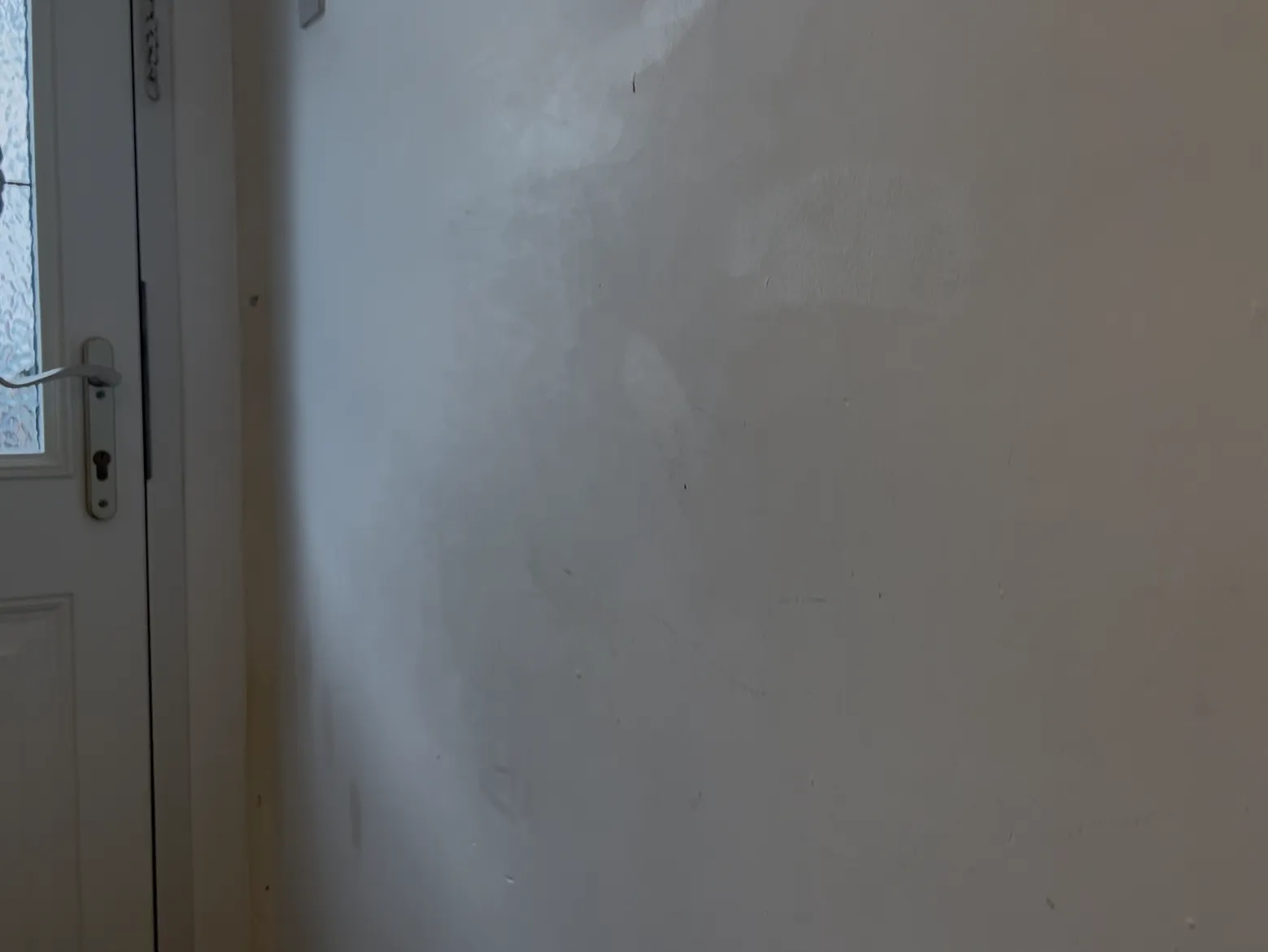 Close-up of plain white hallway wall before custom wood panelling installation showing wall scuffs and unevenness