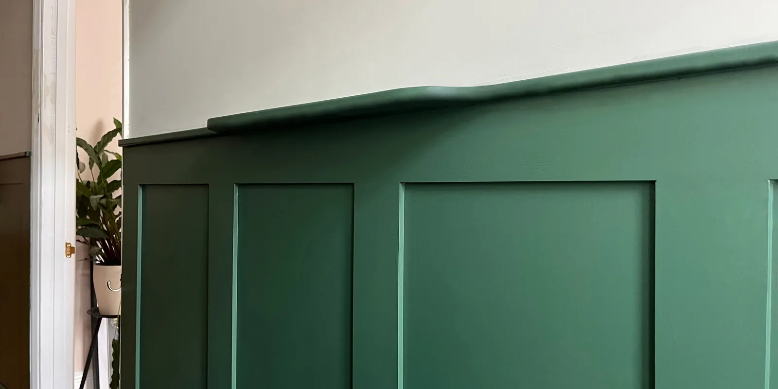 Close-up of deep forest green wainscoting wall panelling with top shelf ledge along a hallway wall