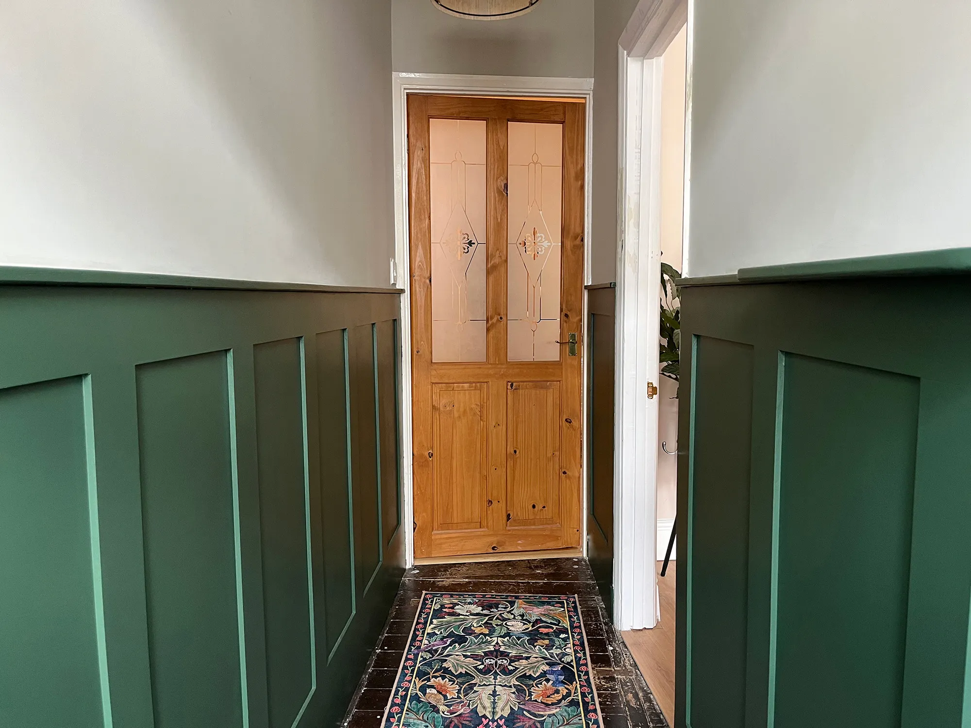 Hallway interior featuring custom dark green shaker style wall panelling, patterned runner rug, and wooden door