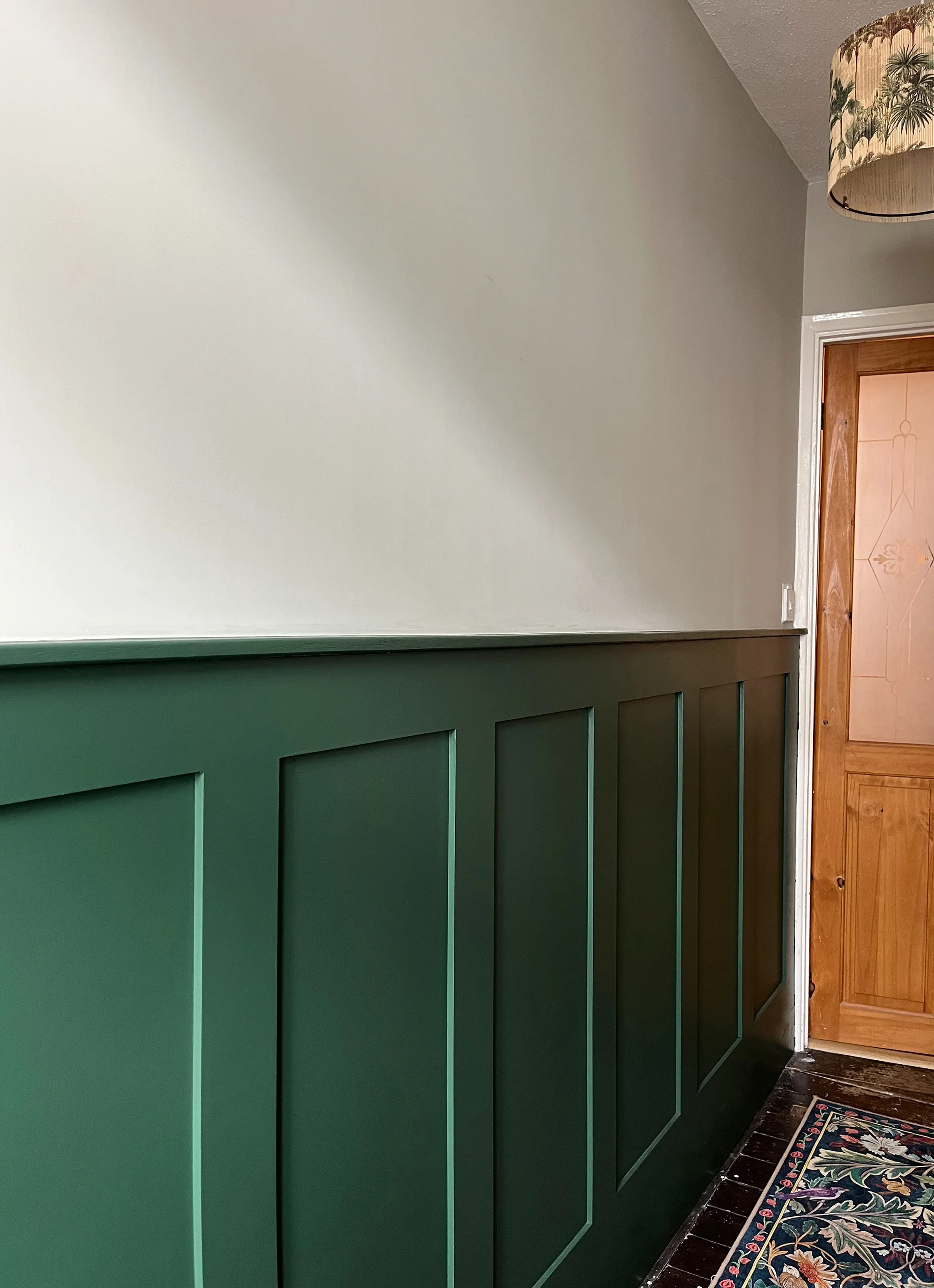 Dark green wainscoting along a hallway wall paired with neutral grey beige upper wall paint