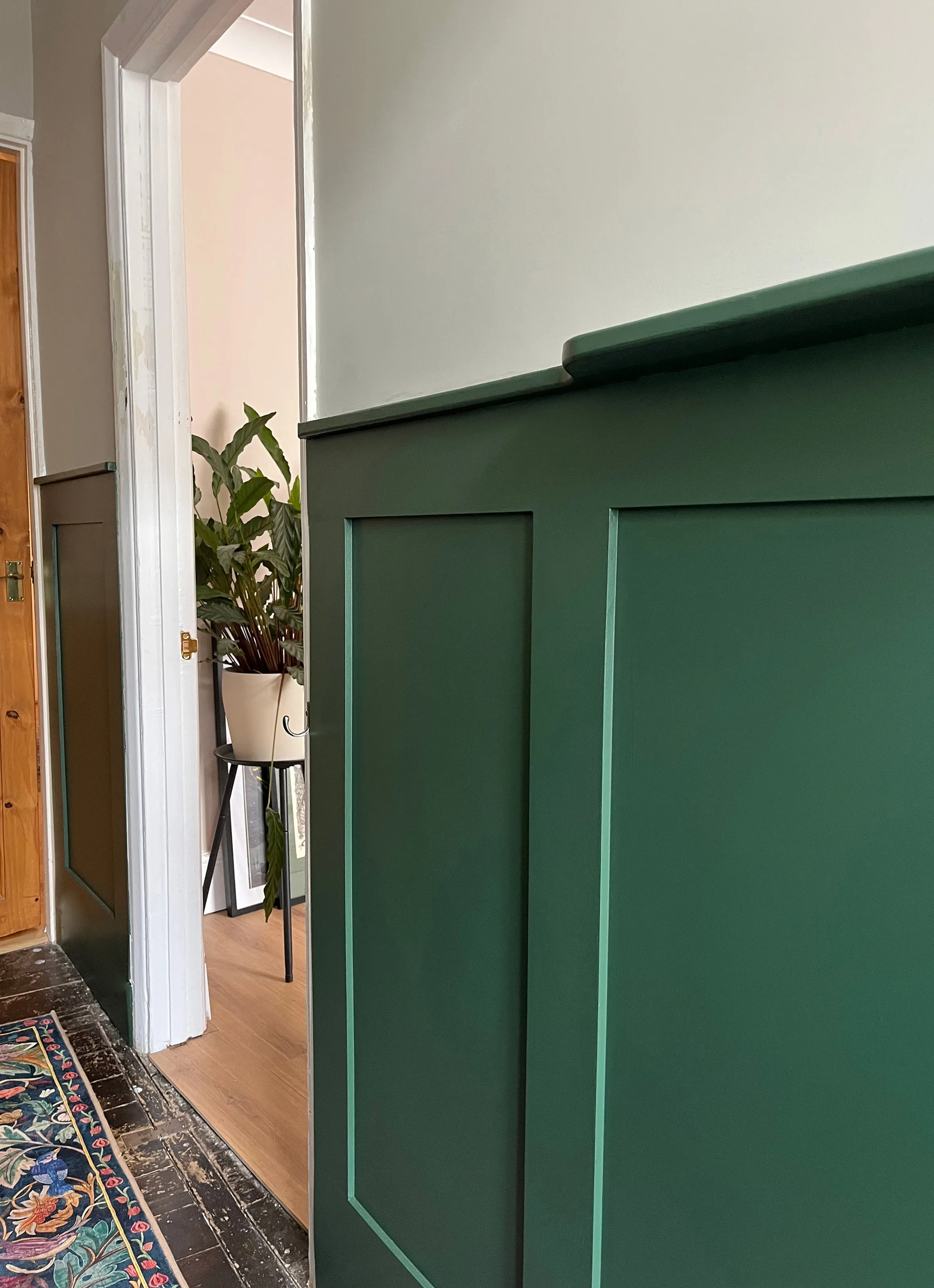 Side profile view of custom green wall panelling with top ledge trim leading into an adjacent room