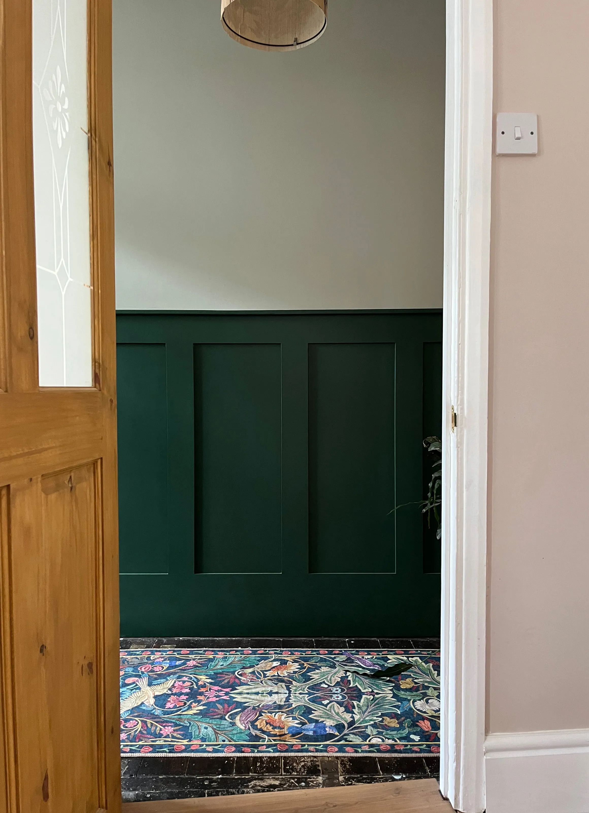 View through a wooden doorway showing custom forest green hallway wall panelling and patterned rug