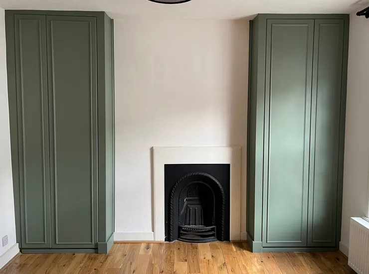 Green built-in wardrobes either side of a fireplace