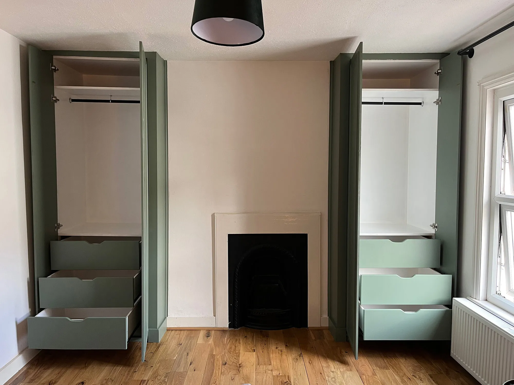 Pair of built in alcove wardrobes showing open doors and three open drawers in a staggered opening in Blackheath