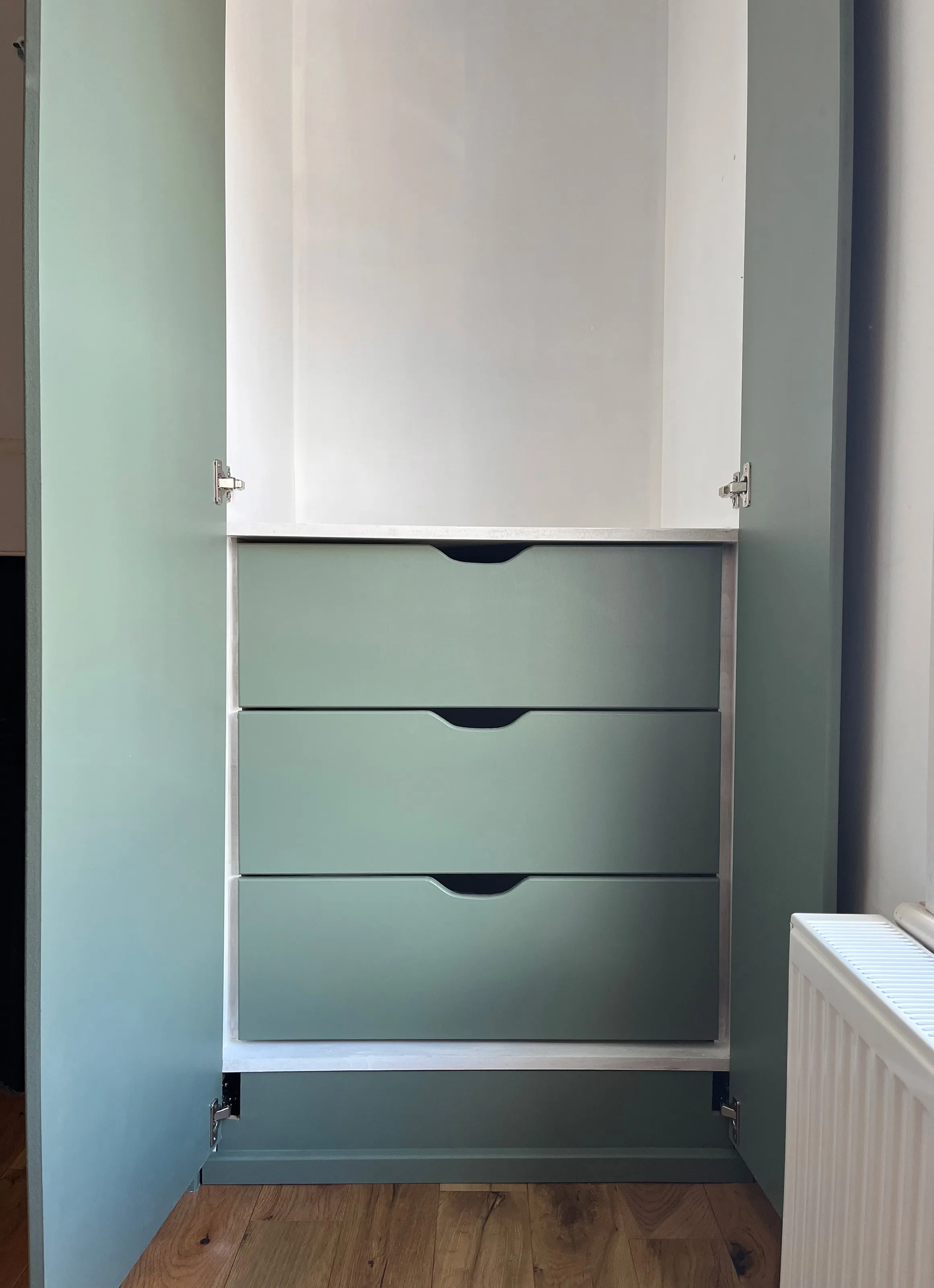 Close up of the inside painted finish of the built in wardrobes showing the green drawer fronts and white carcass interior